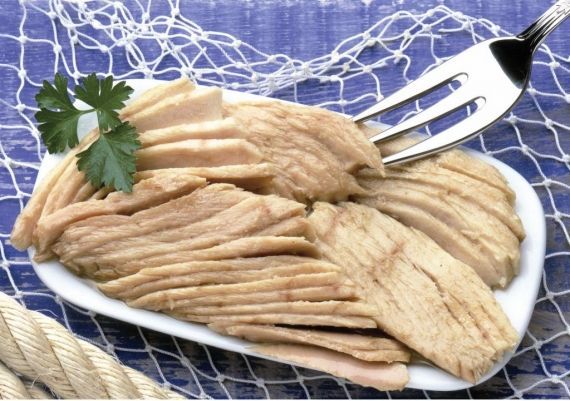 Lonchas de atún cocido en un plato blanco, adornadas con una ramita de perejil y servidas con un tenedor sobre un fondo de red de pesca azul.