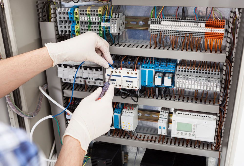 A Person Wearing Gloves is Working on an Electrical Panel — Cairns Synergy Electrical in Manunda, QLD