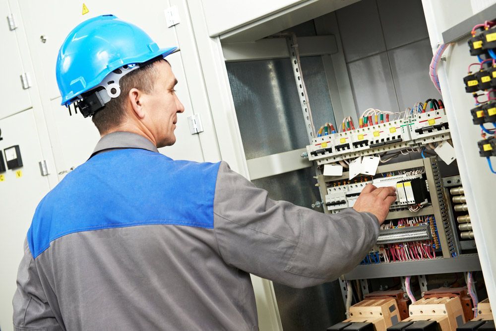 A Man Wearing a Hard Hat is Working on an Electrical Panel — Cairns Synergy Electrical in Manunda, QLD