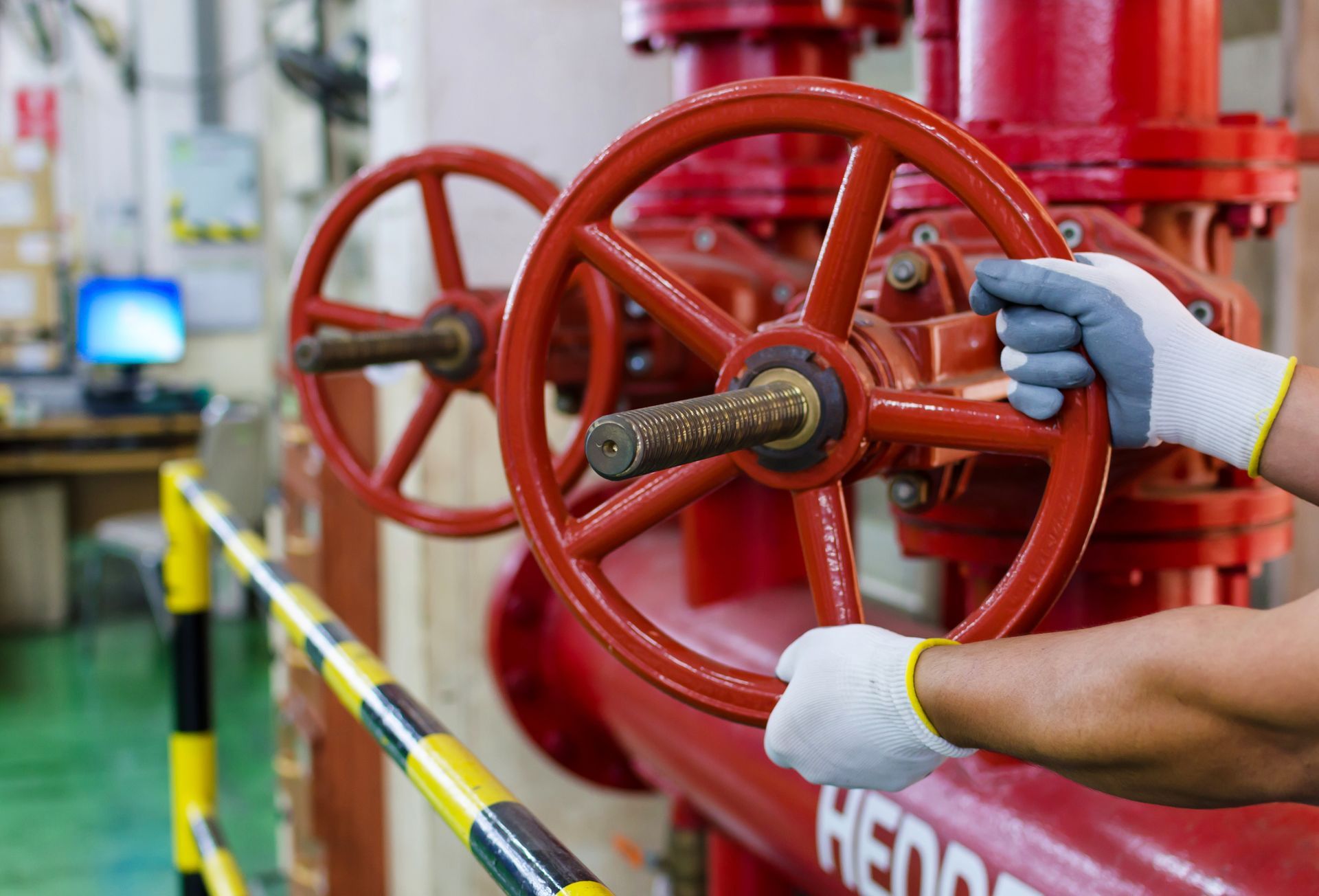 Hands in white gloves turn a red valve wheel on industrial piping.