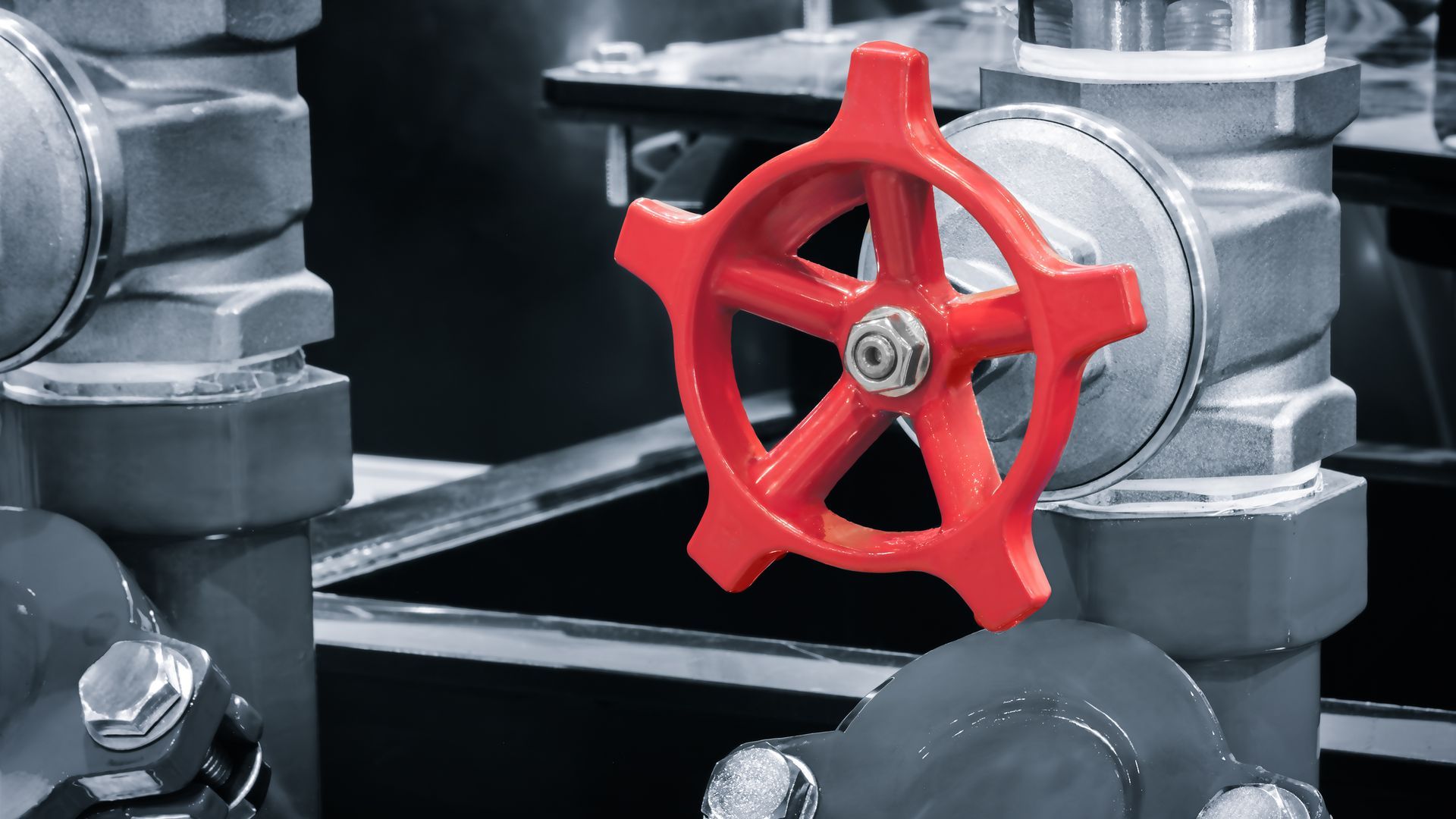Red valve handle on industrial pipes.