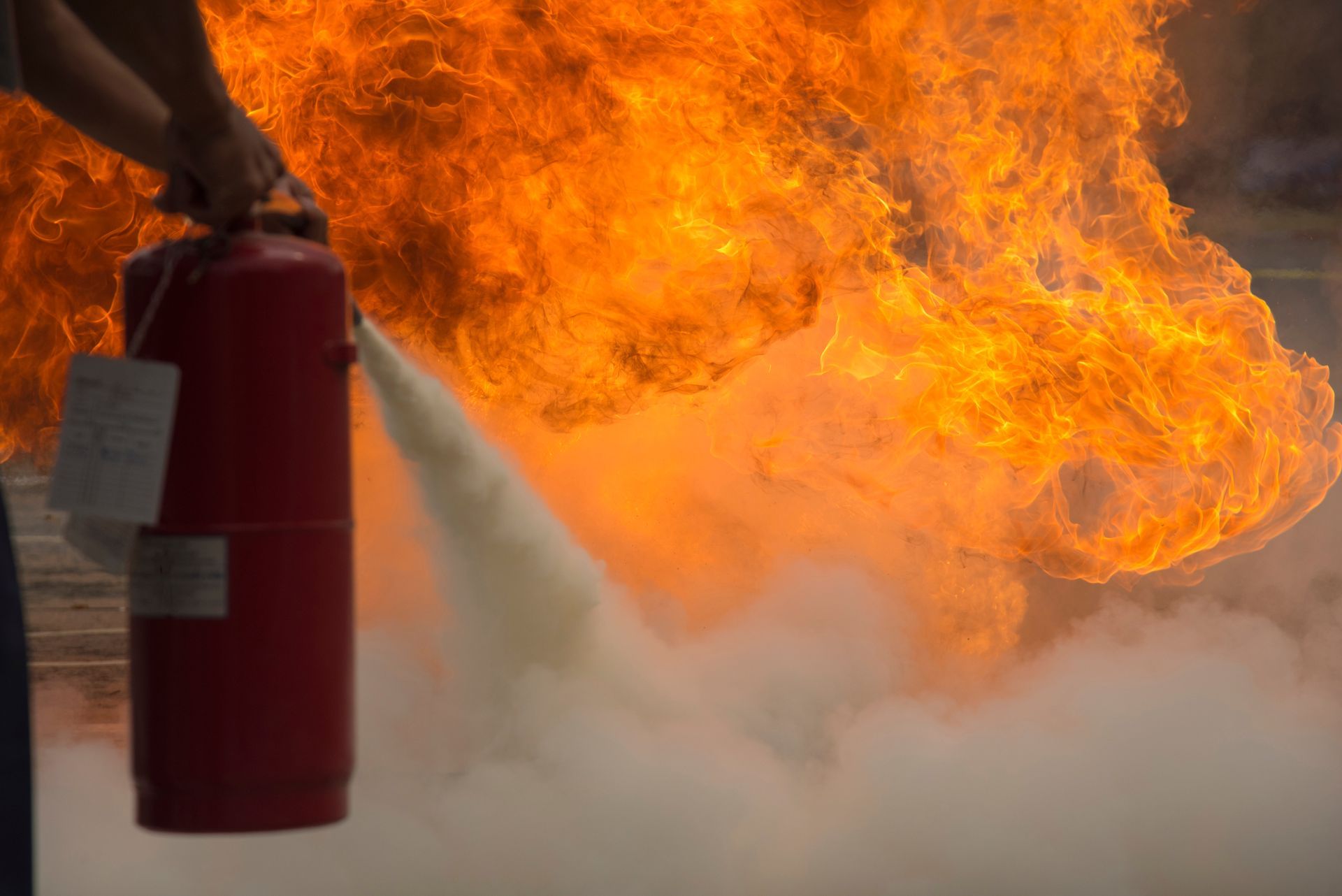 Person using a fire extinguisher on a large fire; orange flames and white extinguishing foam.