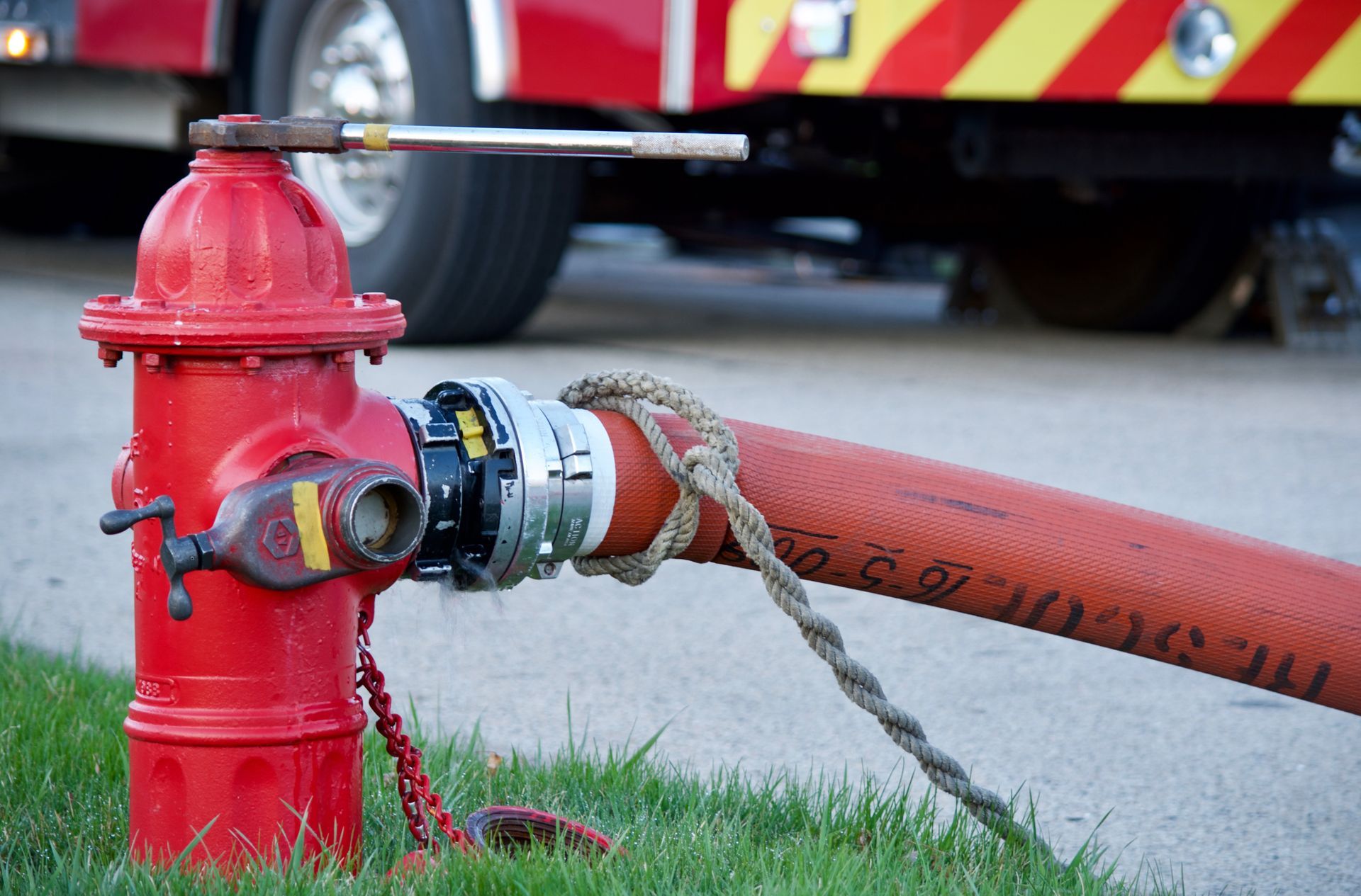 Red fire hydrant with hose attached, next to a fire truck.