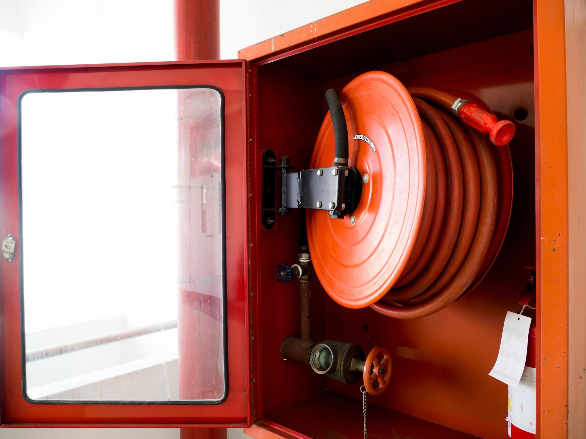 Red fire hose reel inside an open, red cabinet on a wall.