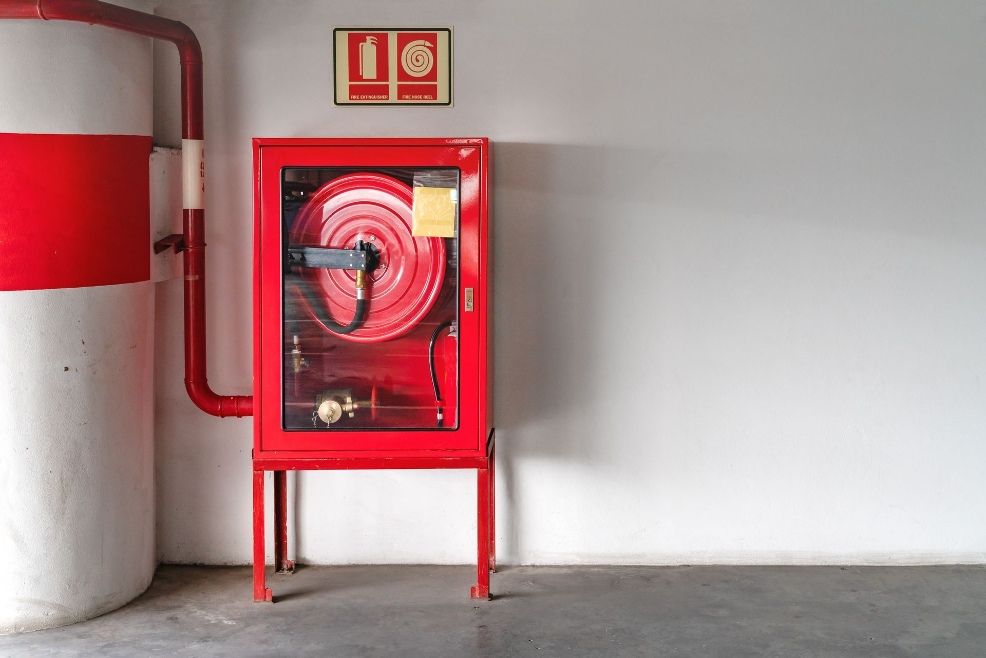 Red fire hose cabinet with a coiled hose and fire extinguisher symbol on a white wall.