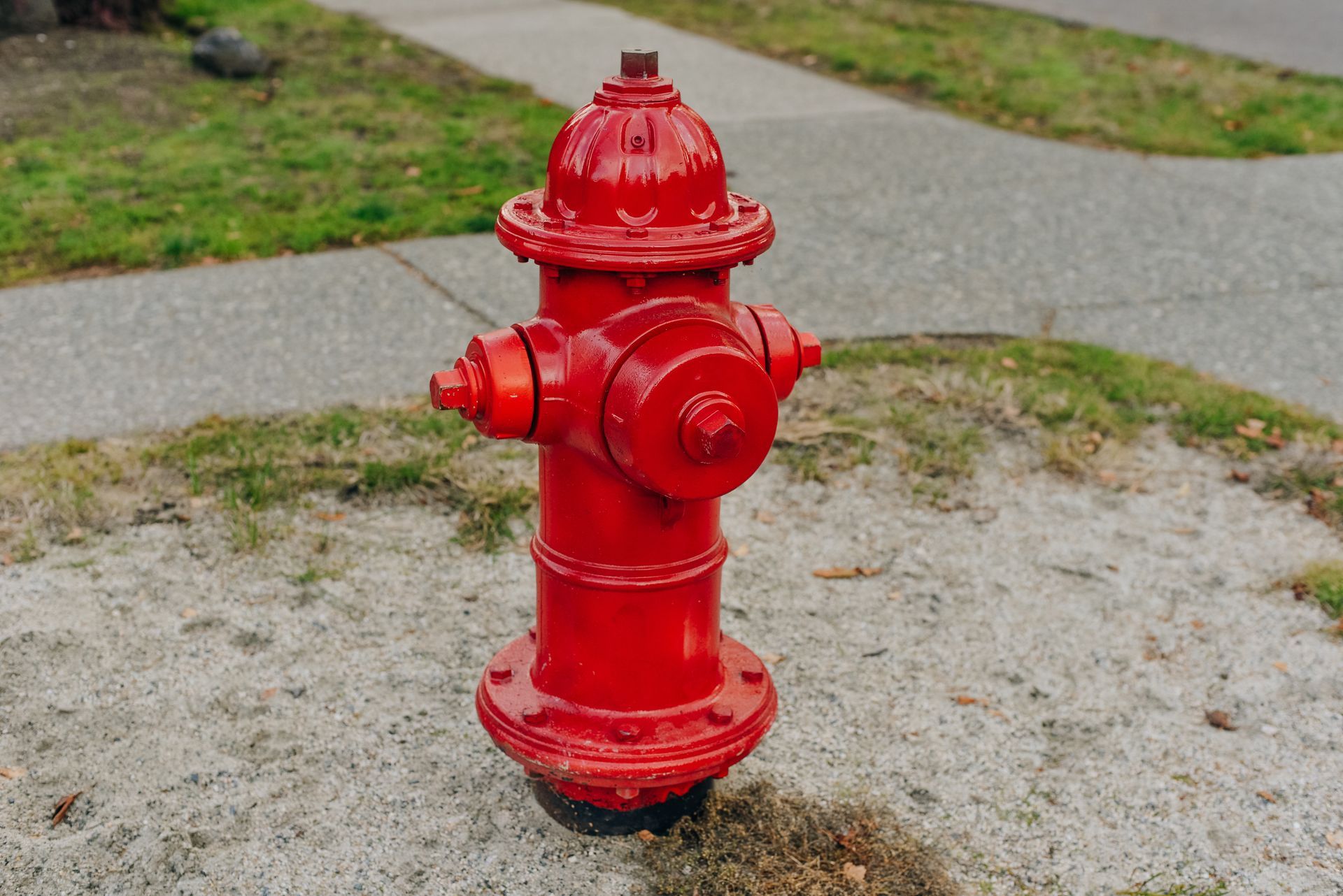Red fire hydrant on a gravel patch beside a sidewalk and grass.