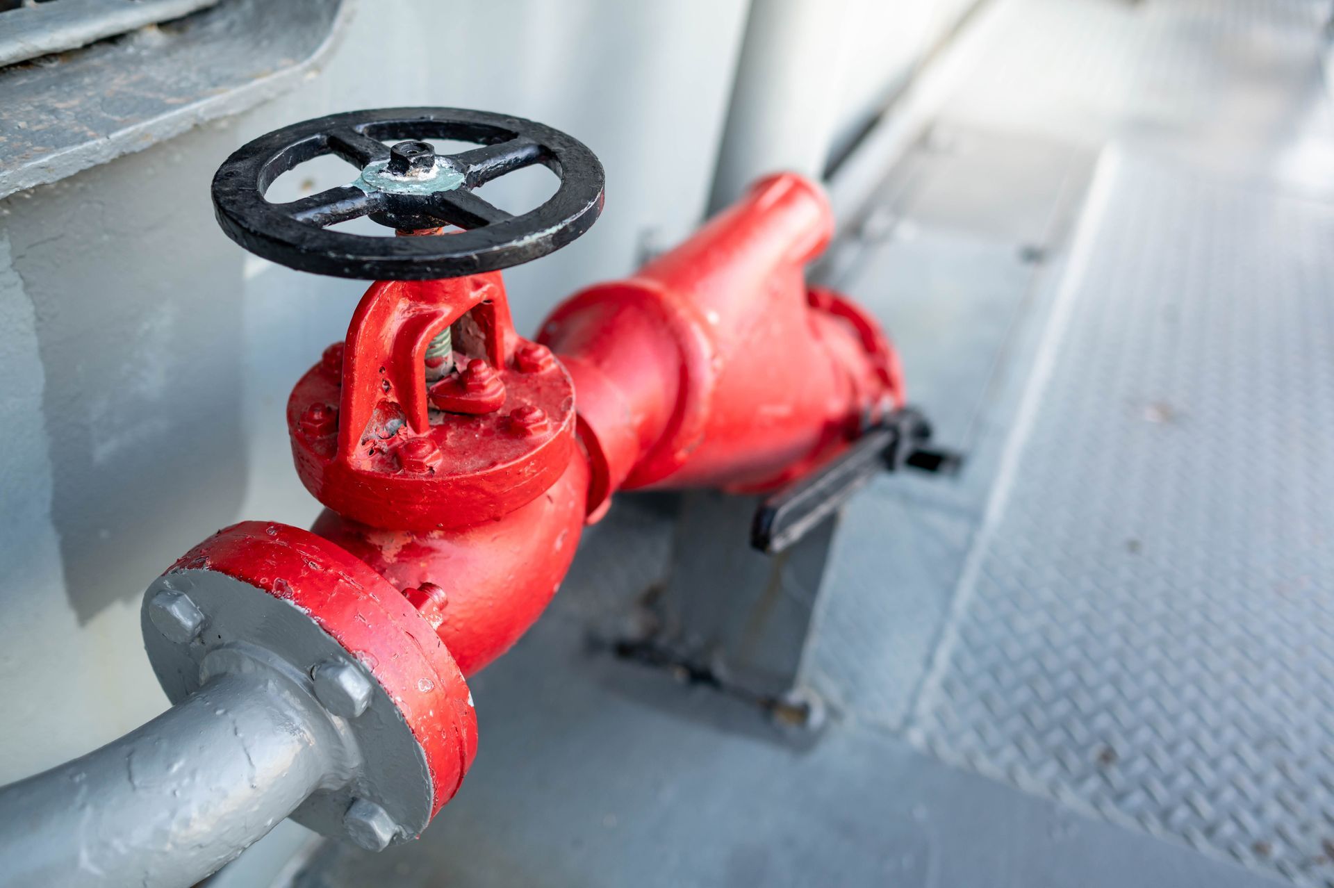 Red fire hydrant valve with a black handle on a silver pipe.