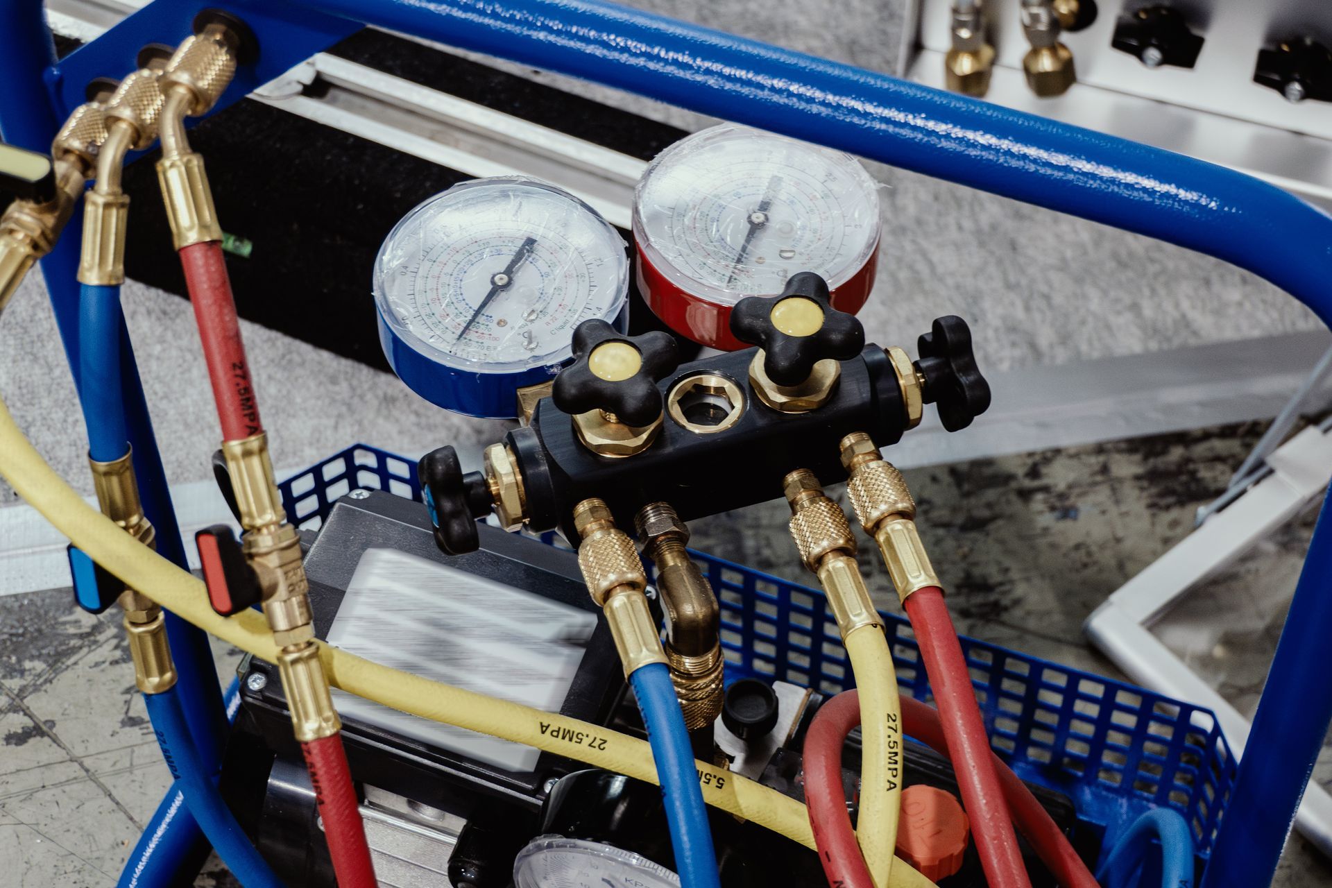 Refrigeration gauges with red, blue, and yellow hoses attached, mounted on a blue cart.