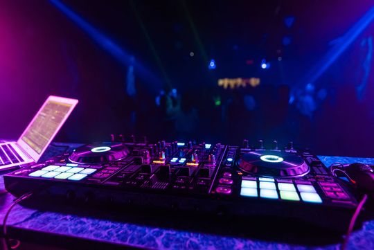 DJ controller with glowing pink and blue lights on a stage in a dark club