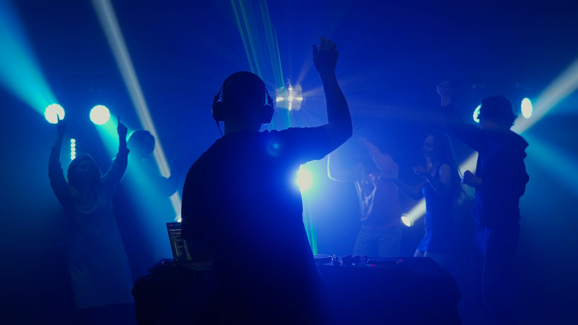 Silhouetted performers on a blue-lit stage with raised hands and spotlights shining through fog