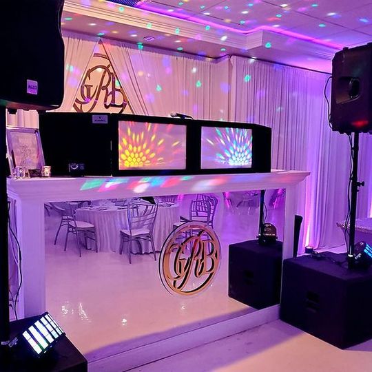 DJ booth with colorful LED screens and purple uplighting at a decorated event venue