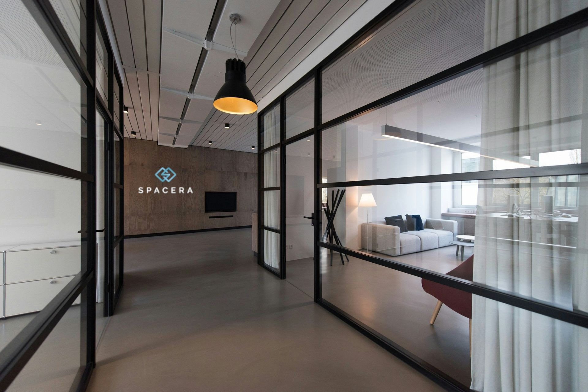 Modern office corridor with glass walls, black metal frames, and hanging pendant lights
