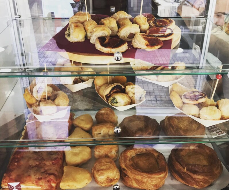 Due cocktail Aperol Spritz con fette d'arancia e cannucce sono serviti su un tavolo di legno insieme a ciotole di patatine e olive.