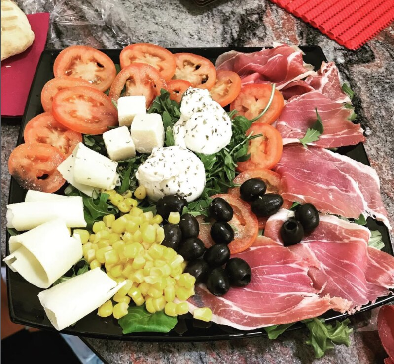 Su un tagliere di legno sono disposte pizze al salame piccante, focaccine al pomodoro e pizzette con olive, servite con patatine e contorni.