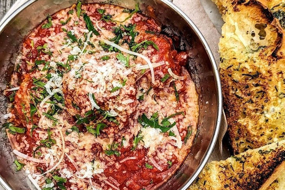 A plate of food with a bowl of sauce and garlic bread on a table.