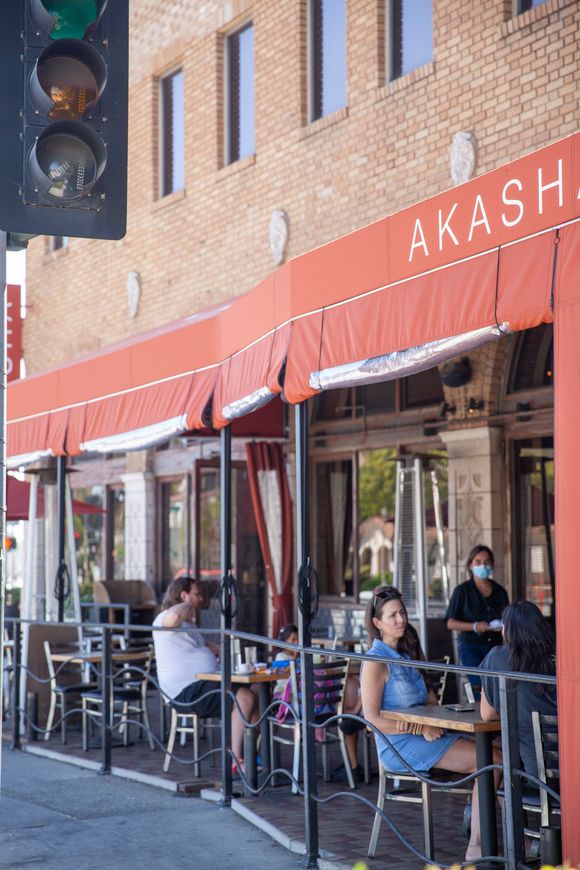 People are sitting at tables outside a restaurant called akash