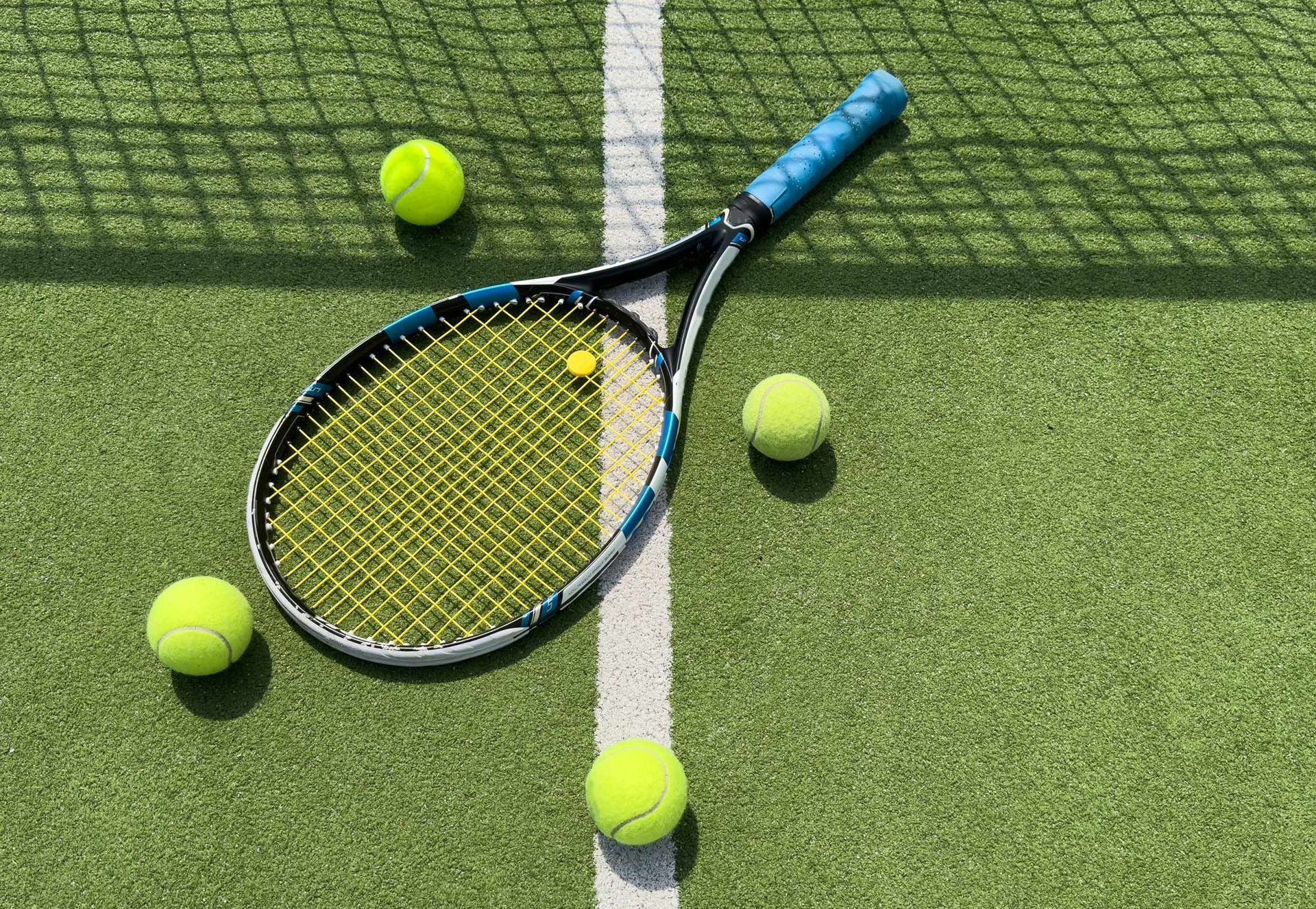 A tennis racket and three tennis balls are on a tennis court.