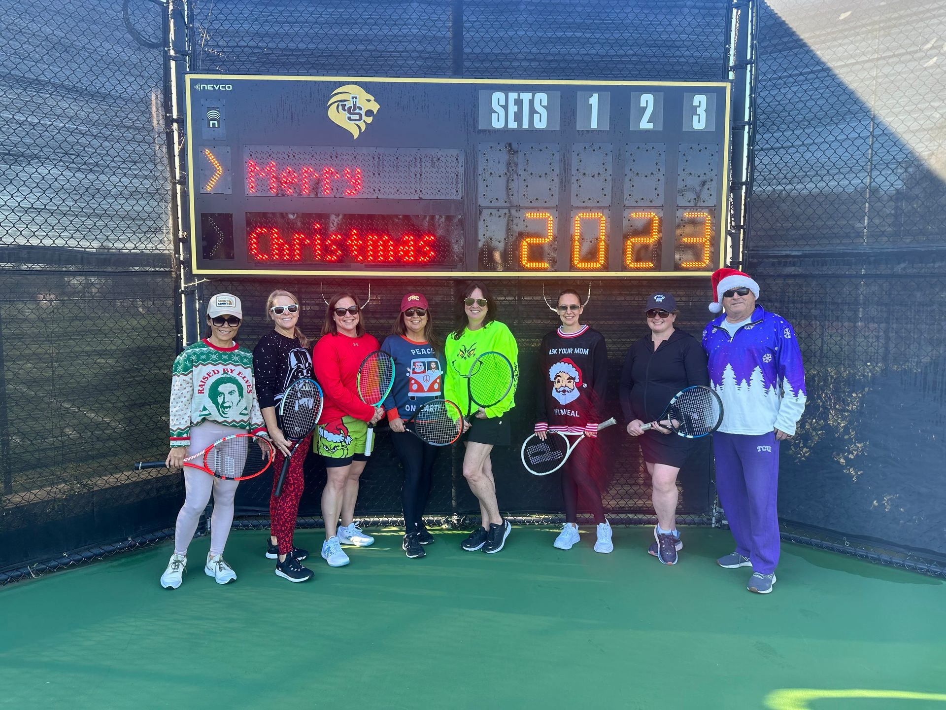 A group of people are standing in front of a scoreboard on a tennis court.
