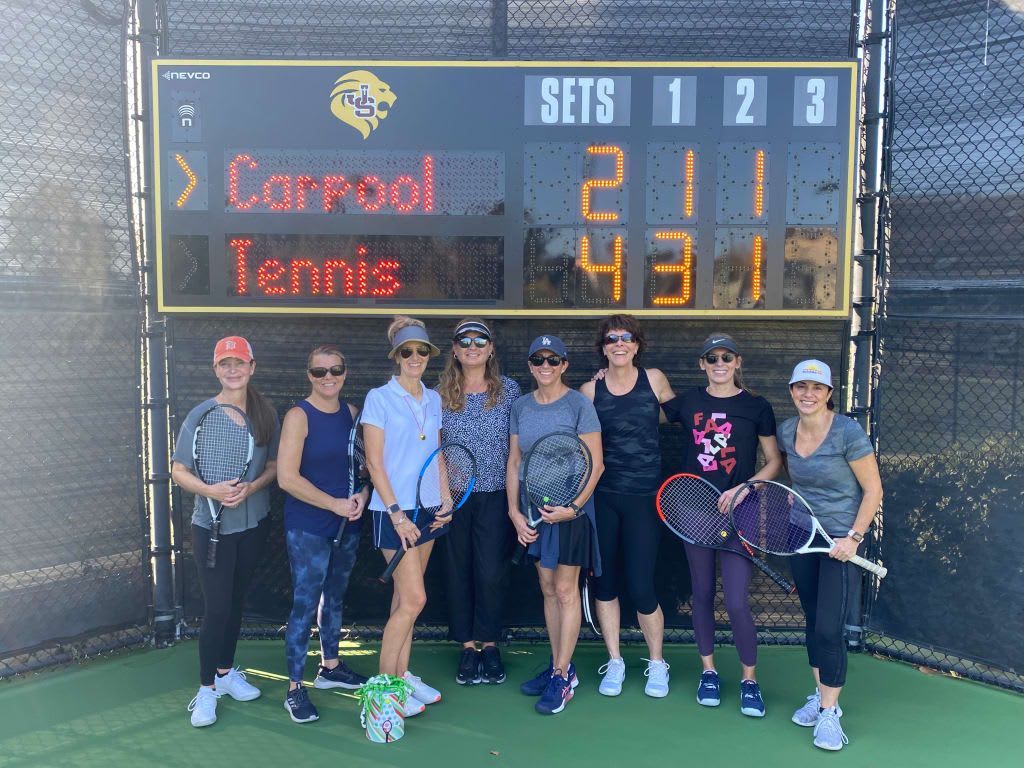 A group of women are standing in front of a tennis scoreboard.