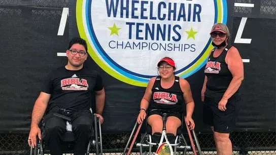 Three people in wheelchairs are standing in front of a sign that says wheelchair tennis championships