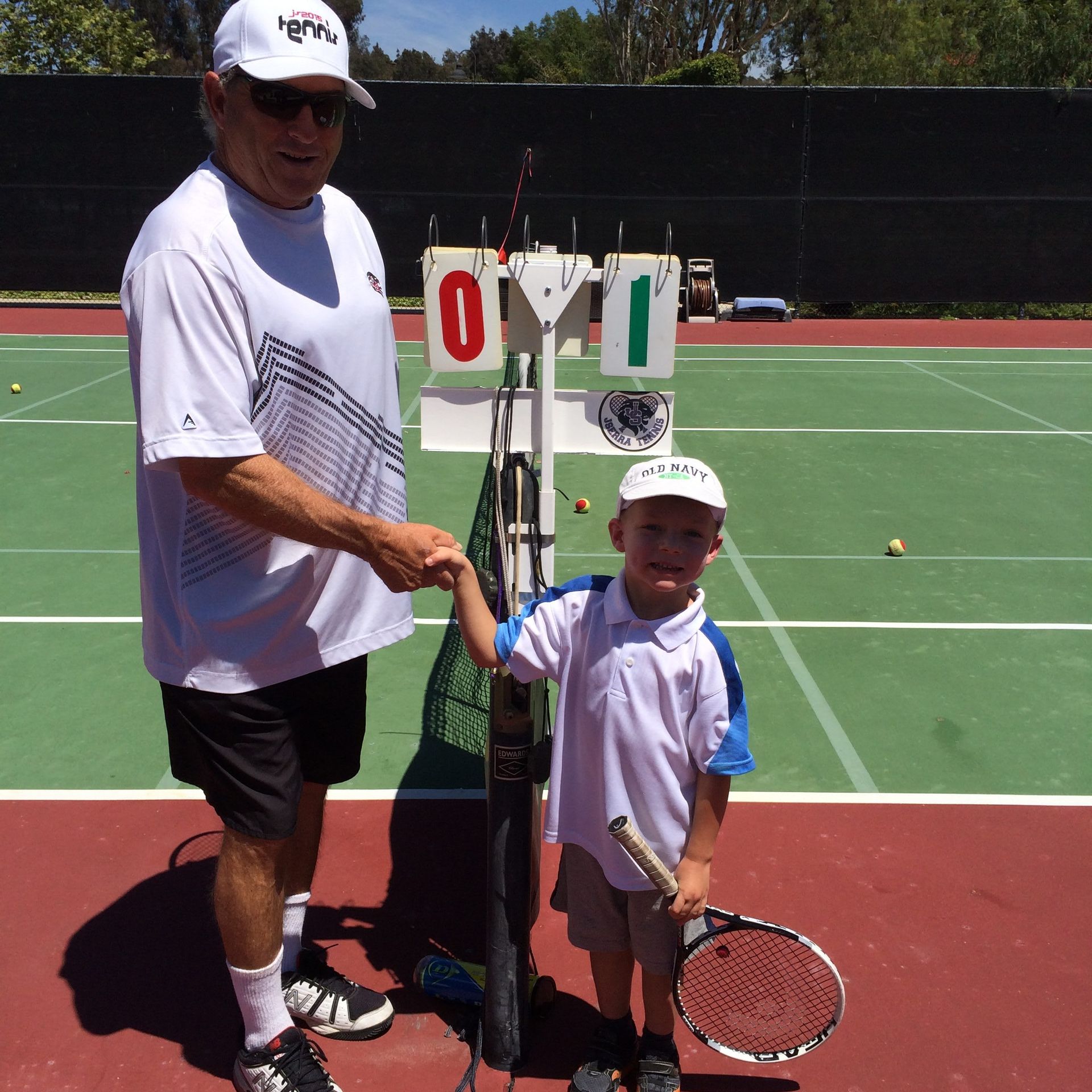A man shakes hands with a young boy on a tennis court