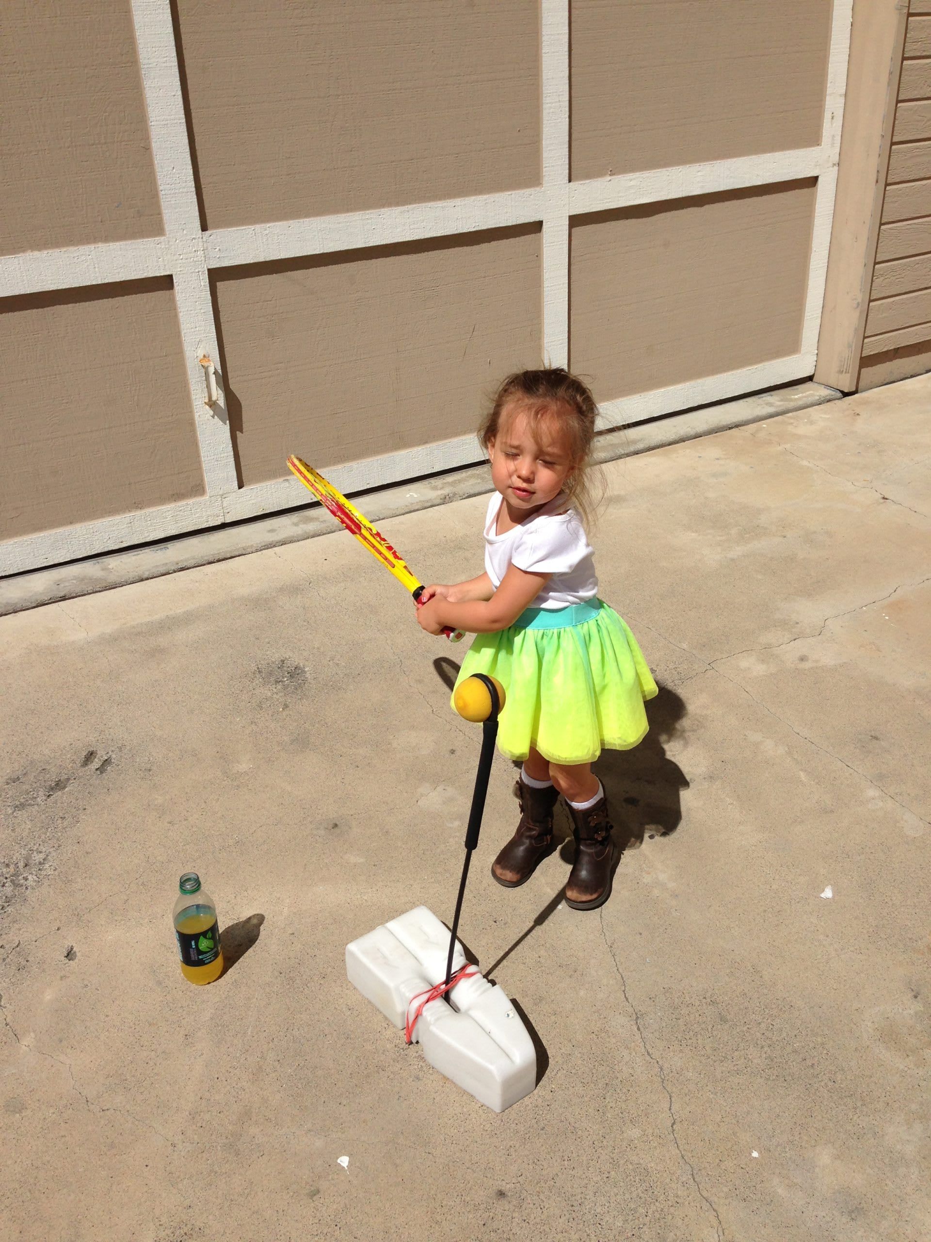 A little girl is playing with a mop in a driveway