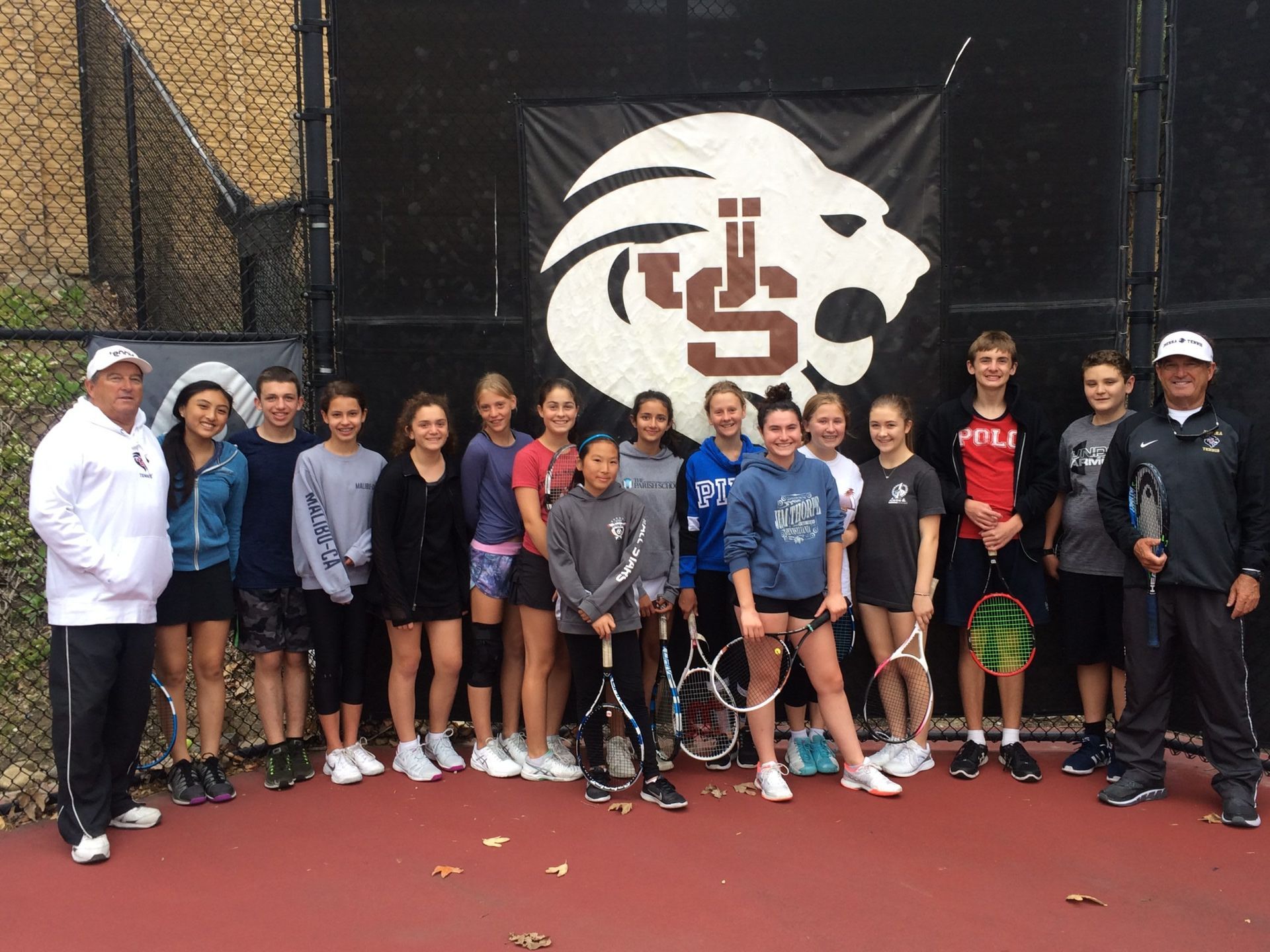 A group of people are posing for a picture on a tennis court.