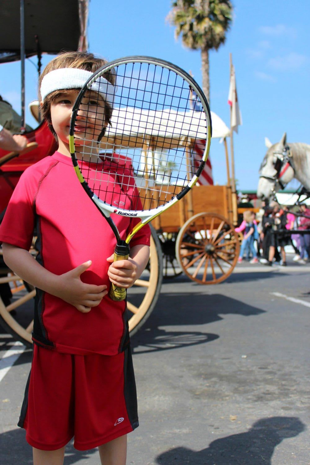A young boy holding a tennis racquet in front of a horse drawn carriage
