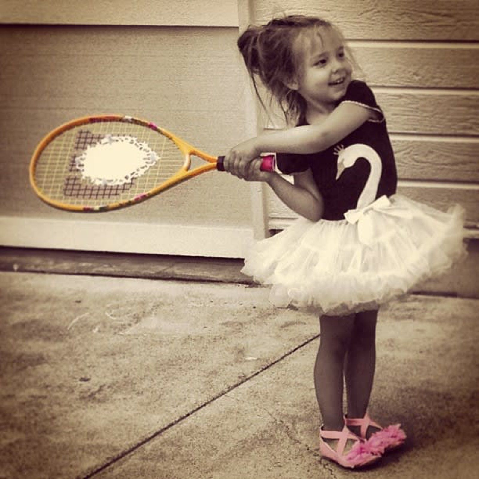 A little girl in a tutu is holding a tennis racquet