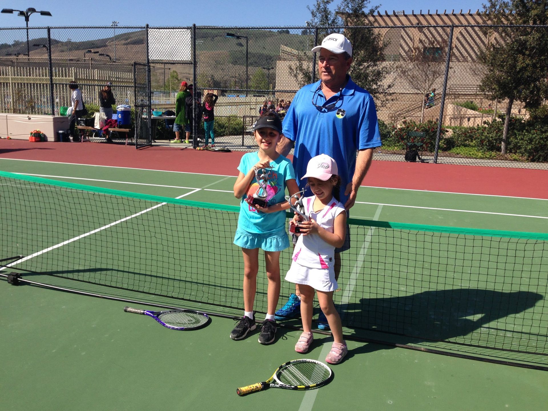 A man and two little girls are standing on a tennis court