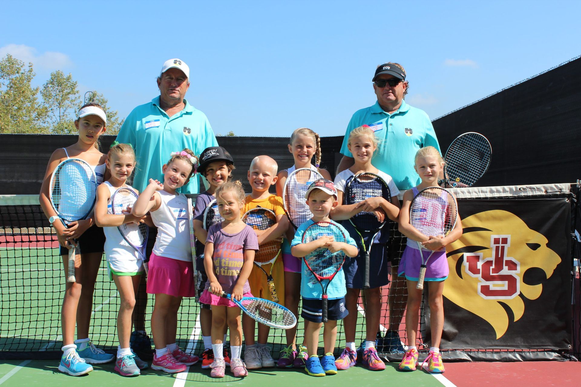 A group of children are posing for a picture on a tennis court.