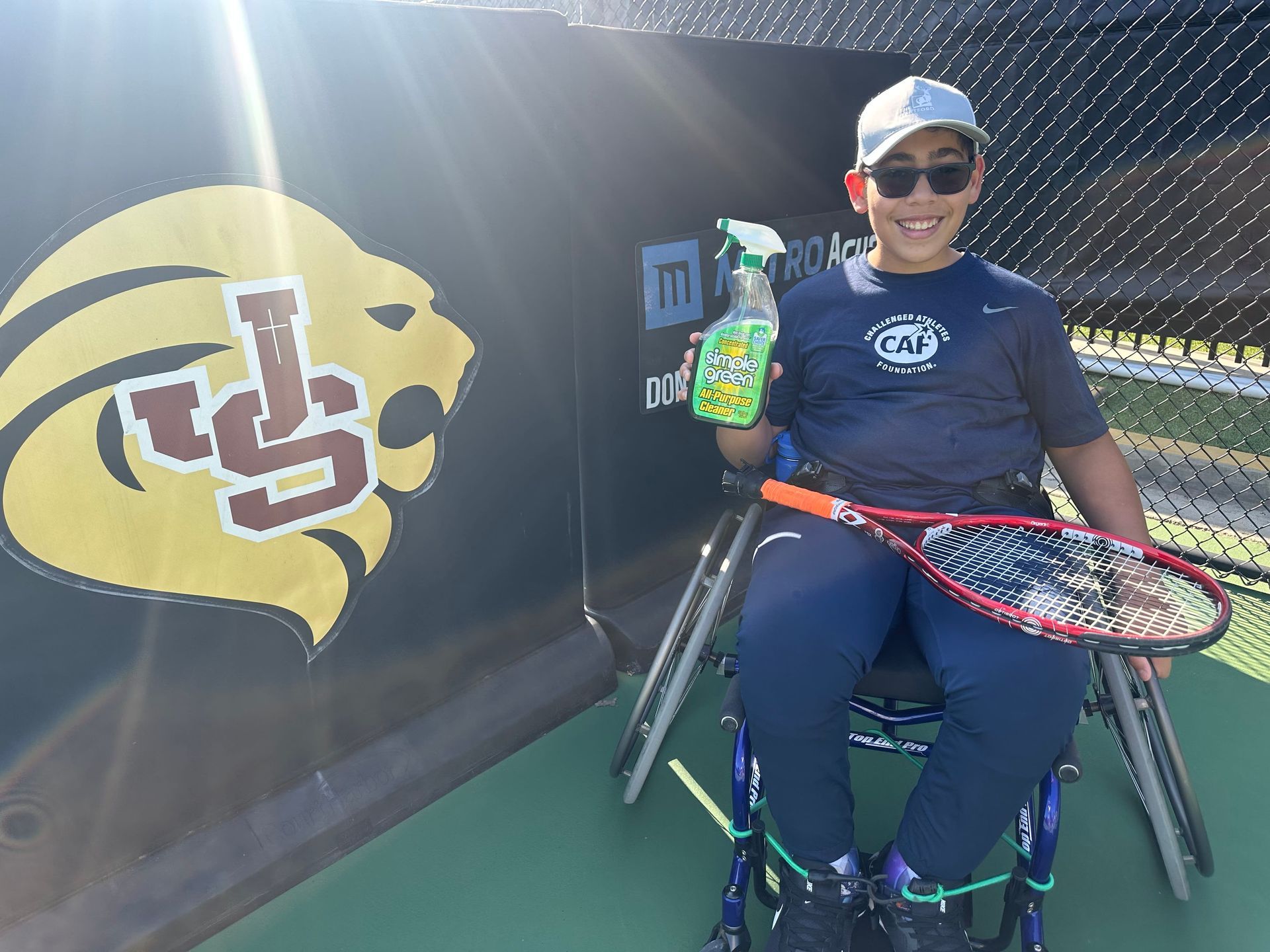 A man in a wheelchair is holding a tennis racquet and a spray bottle.