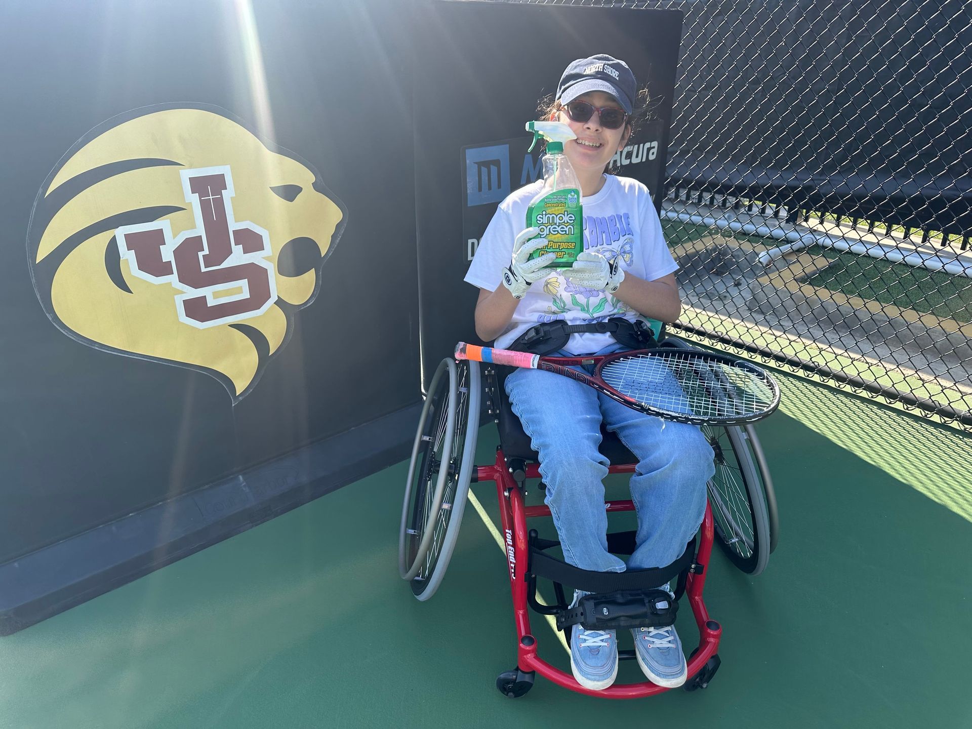 A person in a wheelchair is holding a tennis racquet and a drink.
