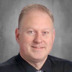 A man in a black shirt and tie is smiling for the camera.