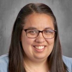 A woman wearing glasses and a blue shirt is smiling for the camera.