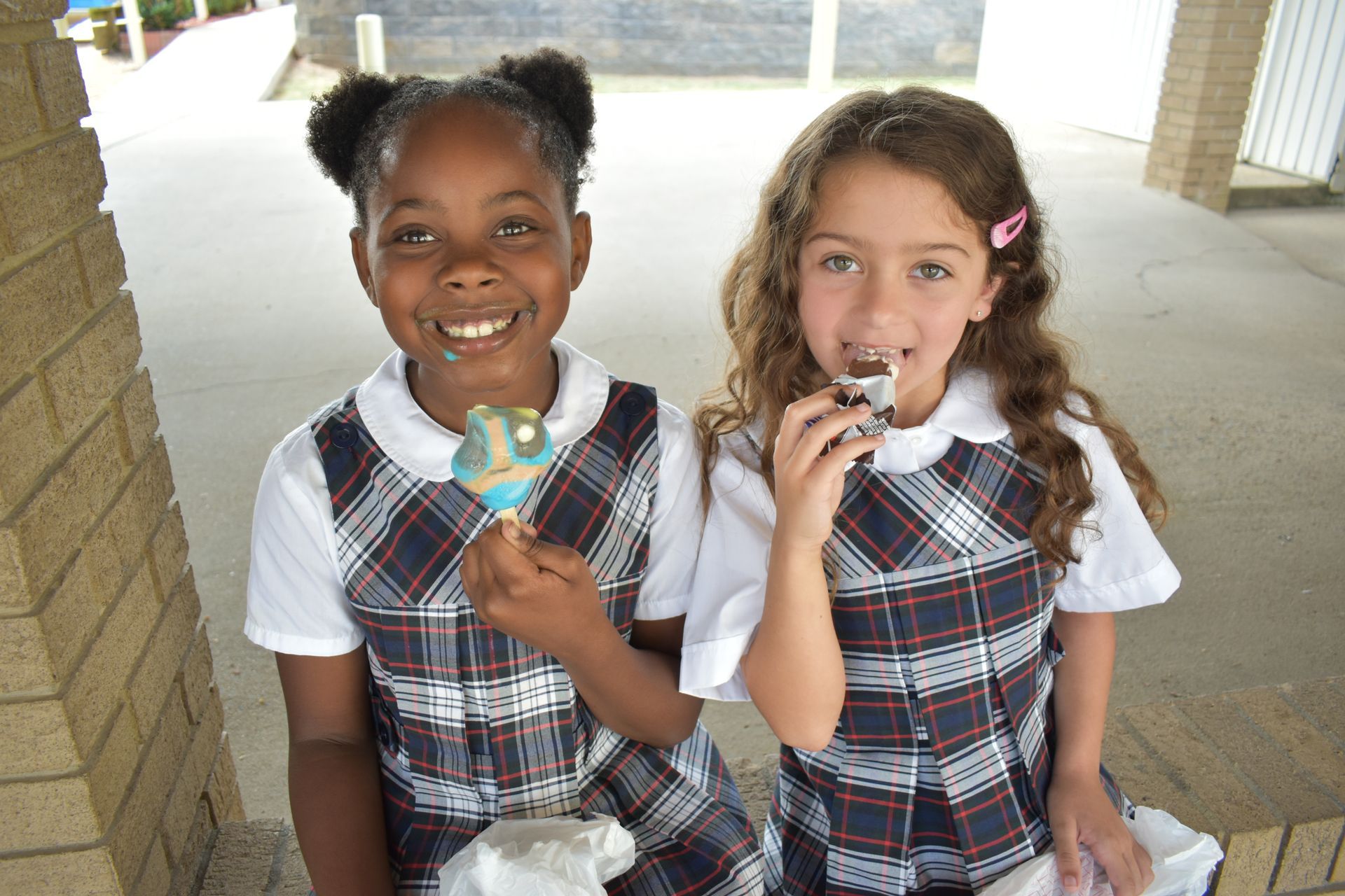 Two young girls are sitting next to each other eating ice cream.