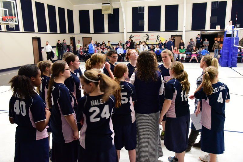A group of girls are huddled together in a gym and one girl has the number 24 on her back