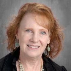 A woman with red hair and a necklace is smiling for the camera.