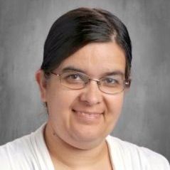 A woman wearing glasses and a white shirt is smiling for the camera.