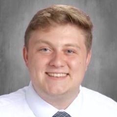 A young man in a white shirt and tie is smiling for the camera.