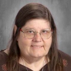 A woman wearing glasses and a brown shirt is smiling for the camera.