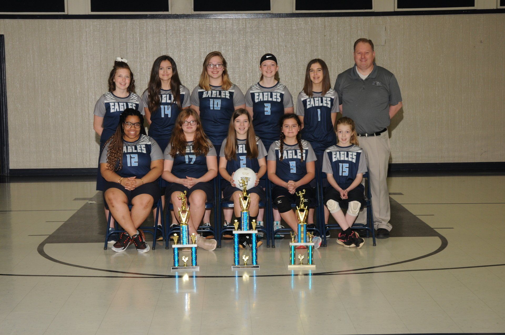 A volleyball team is posing for a picture with trophies.