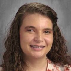 A young woman with curly hair is smiling for a picture.