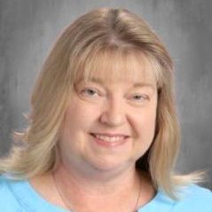 A woman with blonde hair and a blue shirt is smiling for the camera.