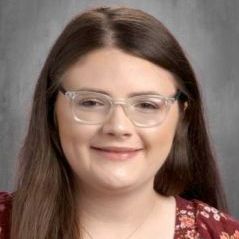 A woman wearing glasses and a red shirt is smiling for the camera.