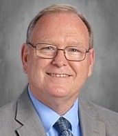 A man in a black shirt and tie is smiling for the camera.