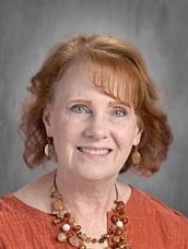 A woman with red hair and a necklace is smiling for the camera.