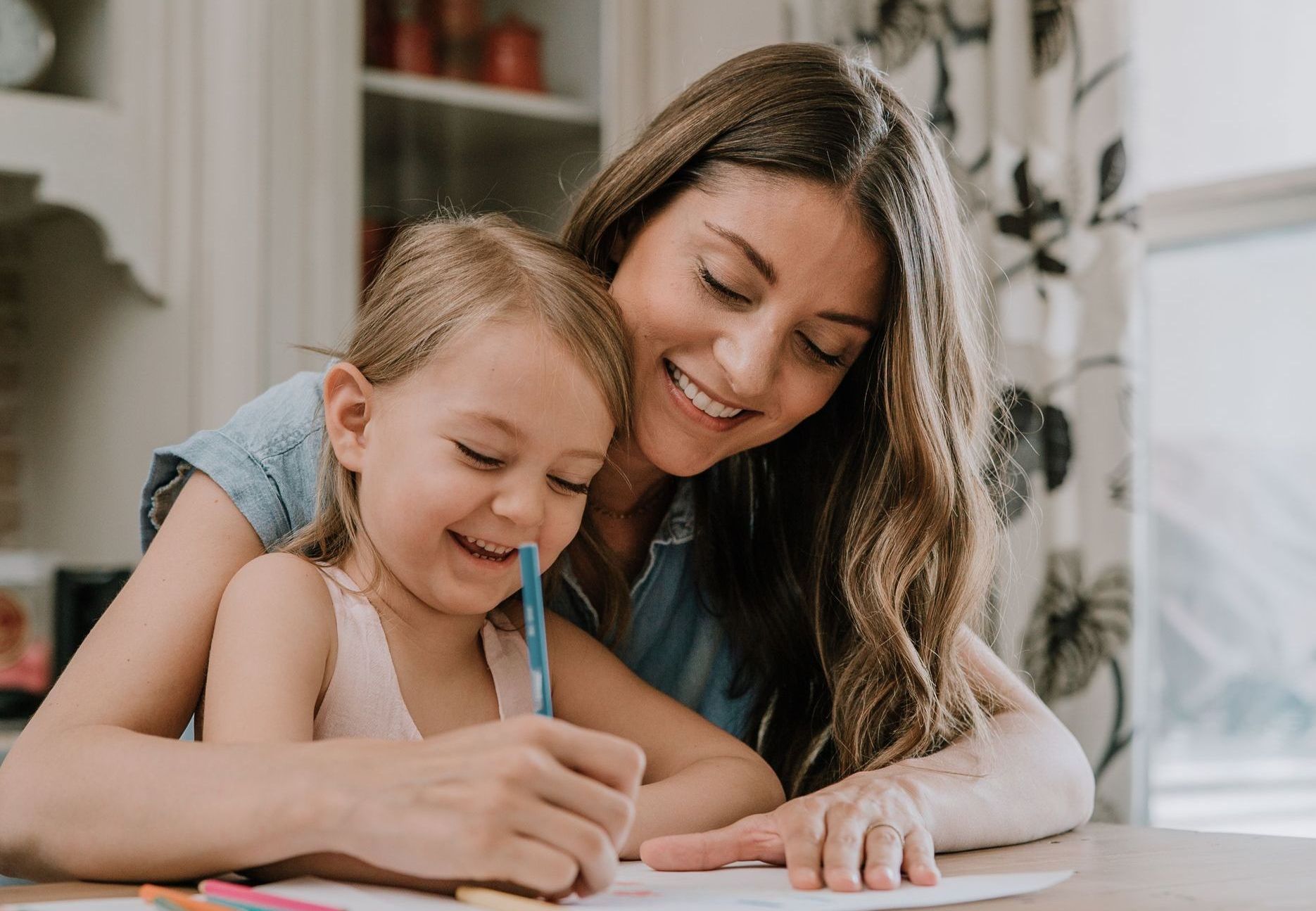 A woman is helping a little girl with her homework at a table.