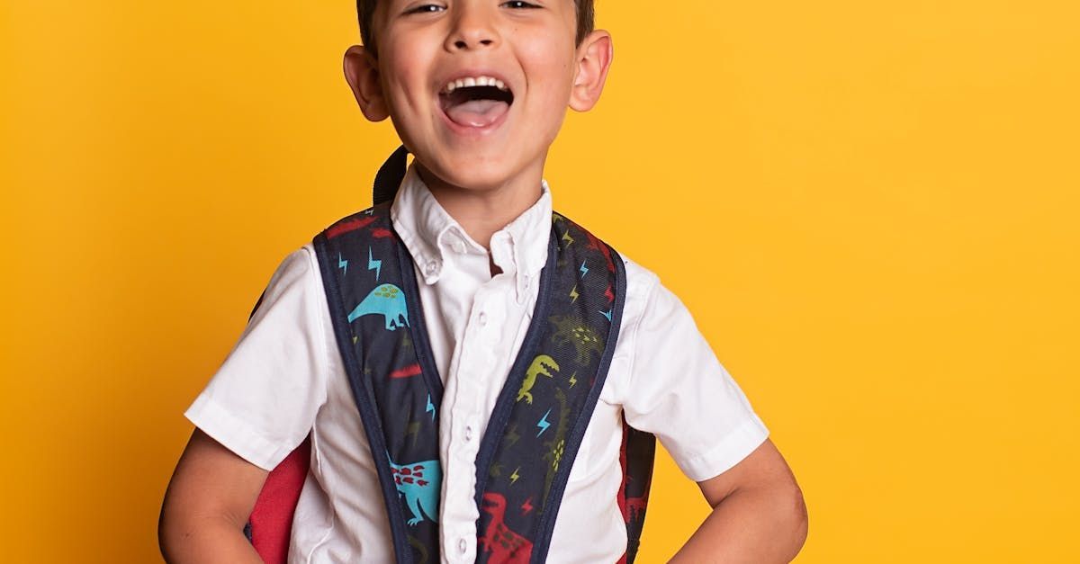 A young boy wearing a white shirt and a backpack is standing in front of a yellow background.