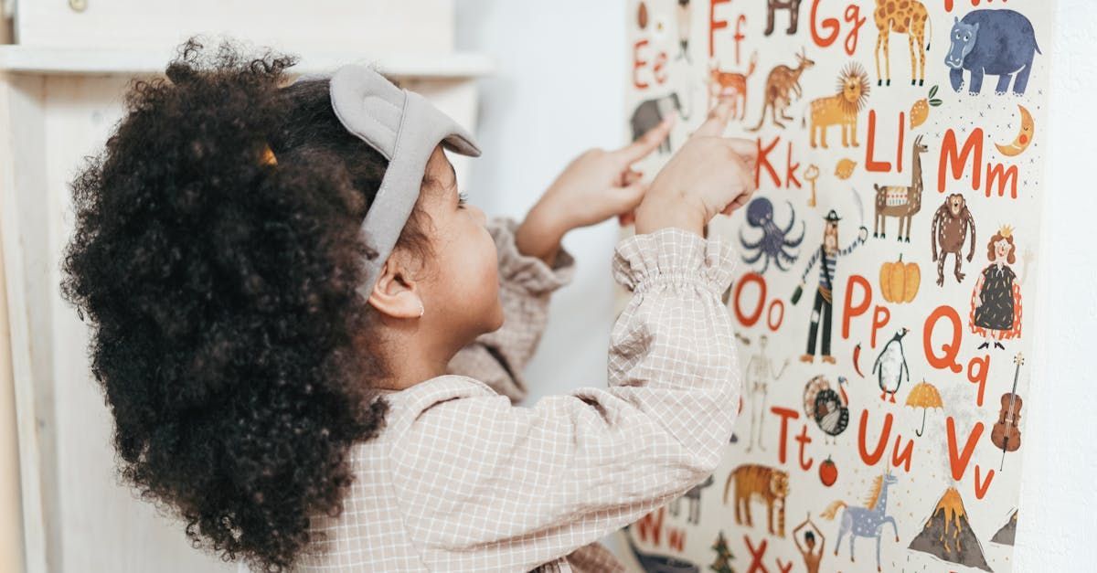 A little girl is pointing at the alphabet on a wall.